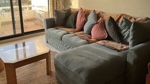A living room with a sectional sofa, a glass coffee table, a large window with curtains, and a framed picture on the wall.