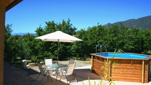 Une terrasse extérieure avec une piscine, une table avec des chaises et un parasol.