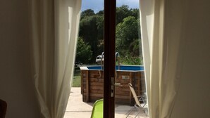 Une pièce dotée d’une porte-fenêtre coulissante donnant sur un espace extérieur avec une piscine et une terrasse en bois.