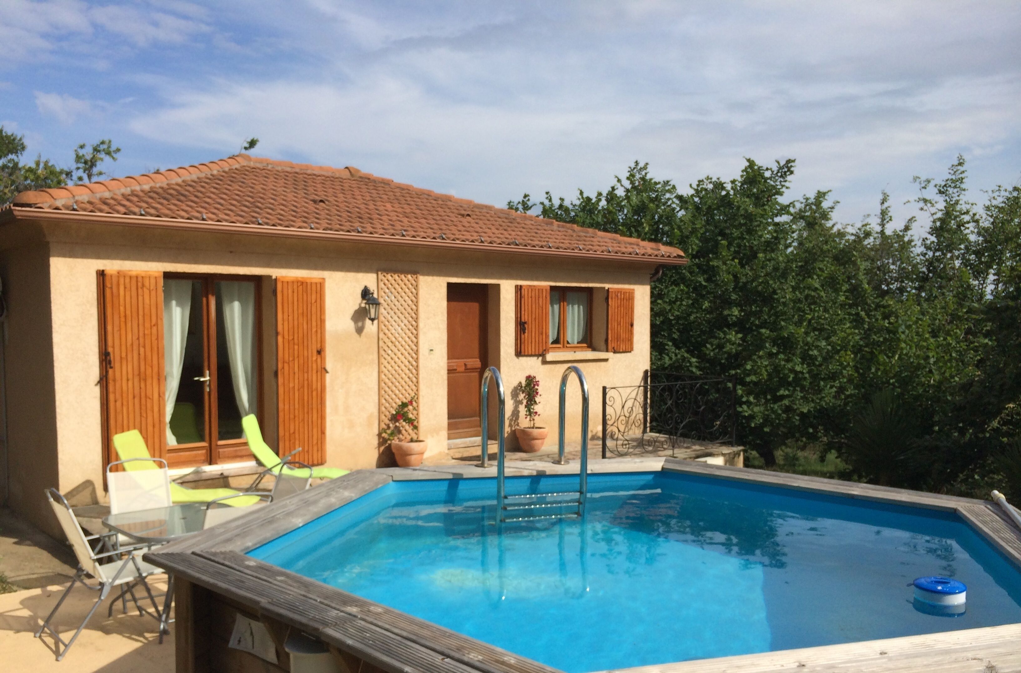 A two-story house with a swimming pool, wooden shutters, and outdoor seating.