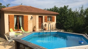 Une maison à deux étages avec une piscine, des volets en bois et un espace salon extérieur.