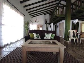 Un salon comprenant un canapé, une table basse avec un plateau en verre, des carreaux de sol à motifs, un escalier et un fauteuil.