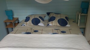 Una cama con cubrecolcha blanco acolchado, almohadas azules y color beige, y un dosel transparente. Hay dos mesitas de noche con lámparas.