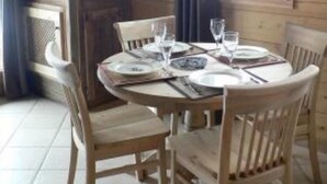 Une salle à manger en bois avec une table ronde dressée pour quatre personnes, entourée de chaises en bois.