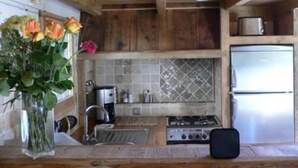 Une cuisine de taille réduite, dotée de meubles en bois, d’un pare-feu en carrelage, d’un réfrigérateur en acier inoxydable et d’une cuisinière à gaz.