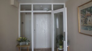 Een kamer met een witte deur, een klein tafeltje met een bloempot en een lijst met een afbeelding aan de muur.