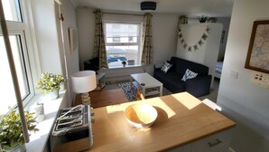 Een compacte leefruimte met kitchenette, een eethoek, een bank en een raam met gordijnen.