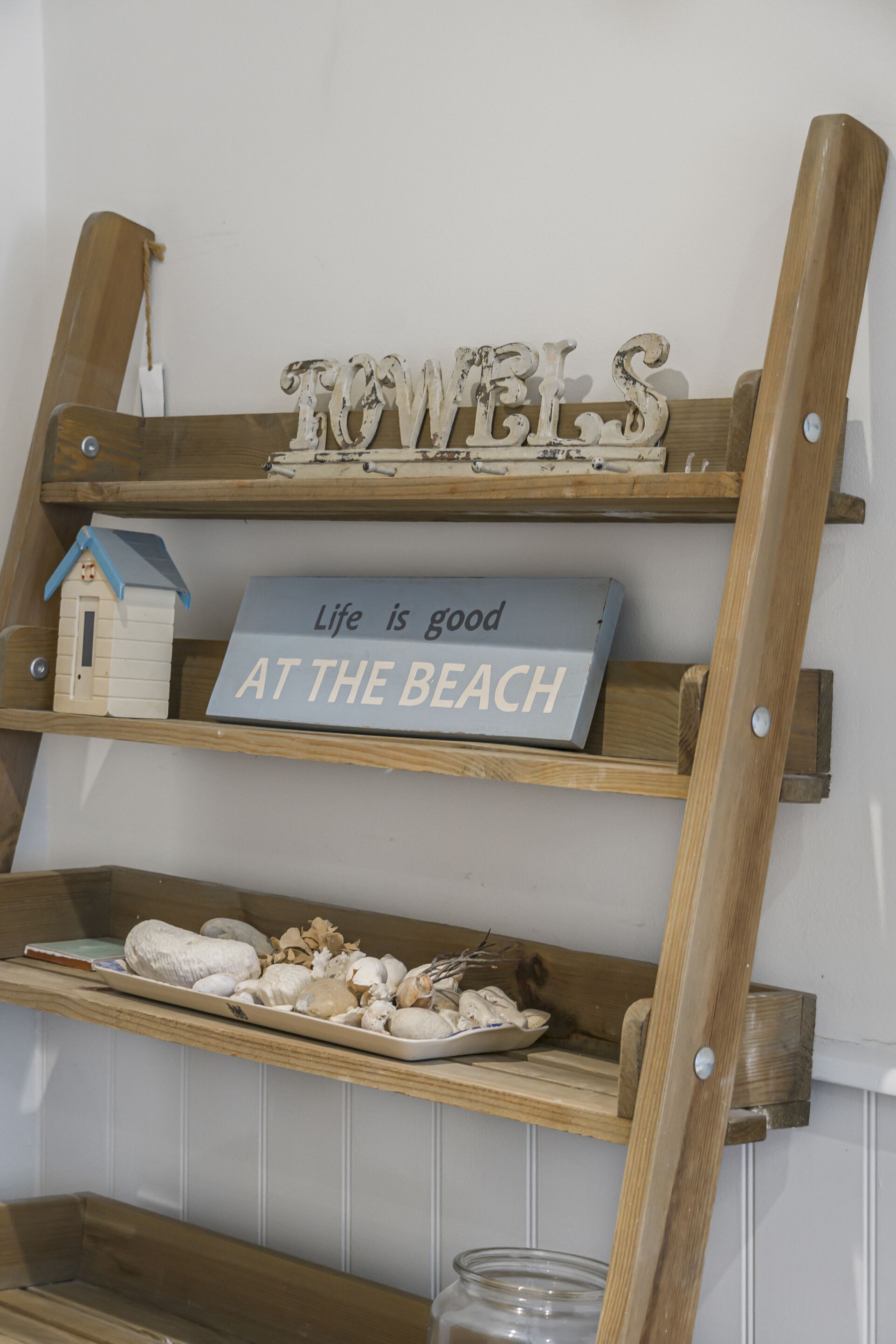Uno scaffale di legno con oggetti decorativi e un cartello con la scritta 'La vita è bella SULLA SPIAGGIA'.