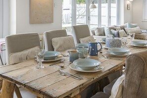 A dining table set with plates, glasses, and cutlery, surrounded by chairs.