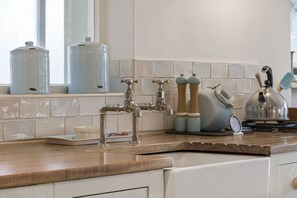 A kitchen with a wooden countertop, stainless steel faucet, and a kettle on the stove.