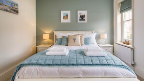 A neatly made bed with a blue and white duvet, two bedside lamps, and two framed pictures on the wall.