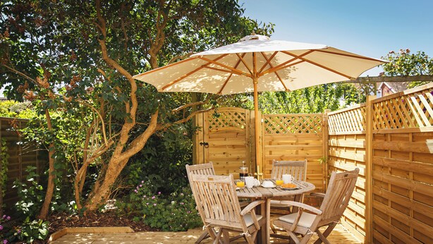 A wooden deck with a table and chairs, surrounded by a wooden fence and lush greenery.