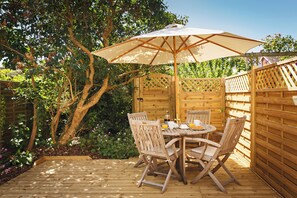 Une terrasse en bois avec une table et des chaises, entourée d’une clôture en bois et d’une végétation luxuriante.