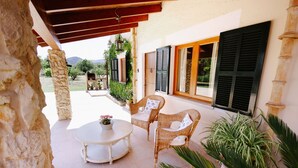 Un patio techado con mobiliario de mimbre, una mesa redonda y plantas en macetas.