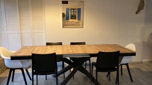 A dining area with a wooden table and black chairs, white chairs, and a wall-mounted picture. - house / villa - 5 rooms - 10/14 persons (Lumio)