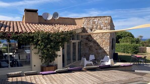 A villa with a wooden deck, outdoor seating, and a stone wall. - house / villa - 5 rooms - 10/14 persons (Lumio)