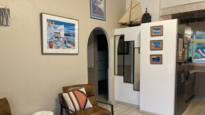 A modern living room with a brown leather armchair, a white sofa, and a dining area with a refrigerator and a window with a view. - house / villa - 5 rooms - 10/14 persons (Lumio)