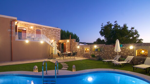 A swimming pool with a ladder, surrounded by a stone wall and a grassy area with lounge chairs. - Blue Paradise villa With Pool And Jacuzzi For 5 People (rethymno)
