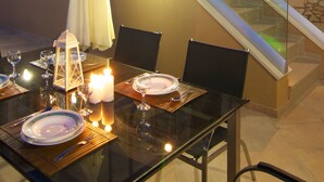 A dining area with a glass table set for two, surrounded by stone walls and a staircase. - Blue Paradise villa With Pool And Jacuzzi For 5 People (rethymno)