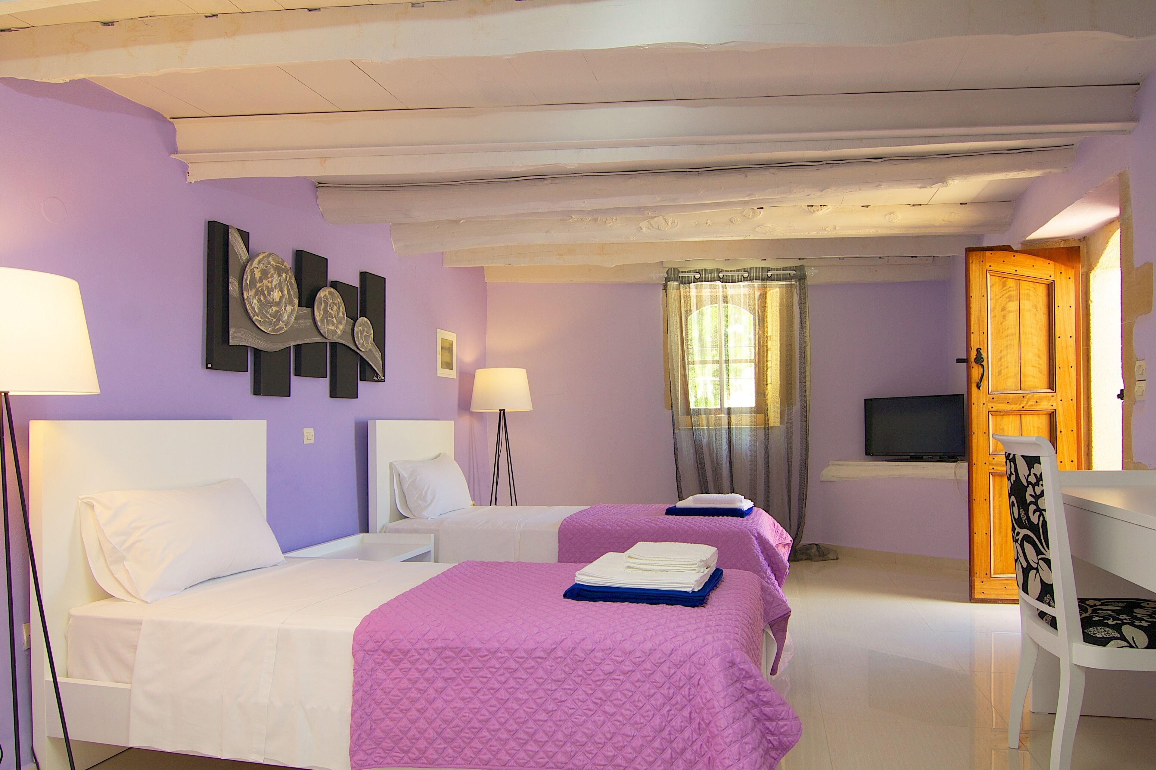 Une chambre d’hôtel avec deux lits, une télévision, une porte en bois et une fenêtre avec des rideaux.