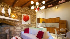 A cozy living room with a stone wall, a fireplace, a white sofa with red cushions, and a dining area with wooden cabinets and a glass table. - Blue Paradise villa With Pool And Jacuzzi For 5 People (rethymno)
