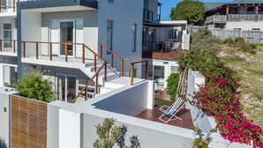 A multi-story residential building with balconies, a wooden deck, and a garden area with flowering plants.