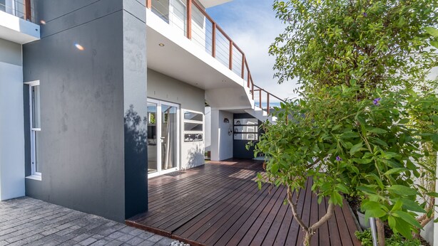 A modern house with a wooden deck, a balcony, and a garden area.