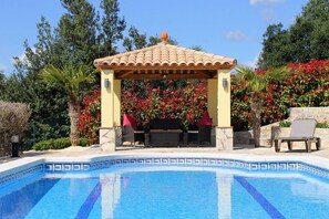 A pool area with a tiled deck, a pergola with a tiled roof, and a seating area with a table and chairs. - Hillside villa, magnificent views, heated private pool, short walk to village (Calonge)