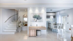 A modern kitchen with a central island, white cabinetry, and a dining area with white chairs.