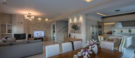 A modern living room with a wooden dining table, a sofa, and a TV. There is a staircase leading to another level.