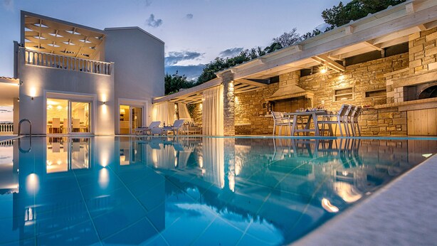 A modern poolside area with a clear pool, outdoor seating, and a stone fireplace.