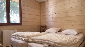 Une chambre avec deux lits, des murs en bois, une fenêtre et un radiateur.