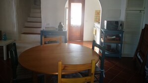 Un coin repas avec une table et des chaises en bois, une cuisine équipée d’un four à micro-ondes et un escalier menant à l’étage supérieur.