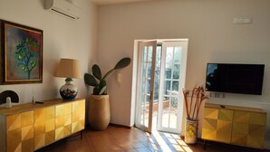 Een woonkamer met een televisie, een schilderij, een lamp en een cactus.