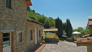 A stone building with a tiled roof, a covered patio area, and a view of a lush green landscape.