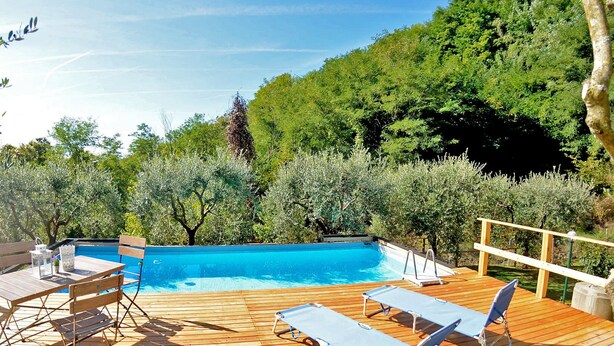 A wooden deck with a swimming pool, lounge chairs, and a table.