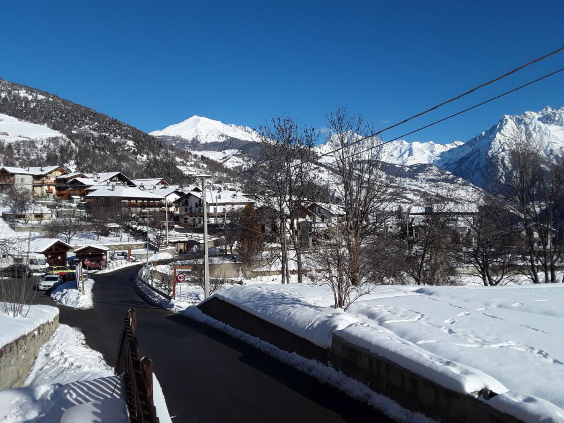 Un pueblo cubierto de nieve en la montaña con edificios tradicionales de madera, una carretera despejada y un cartel de límite de velocidad de 50 km/h.