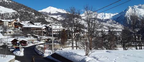 Un pueblo cubierto de nieve en la montaña con edificios tradicionales de madera, una carretera despejada y un cartel de límite de velocidad de 50 km/h.