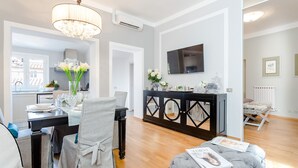 A modern living room with a dining area, a black console table with decorative items, and a grey ottoman with magazines. - Flourish Apartment with Grand Terrace inside Lucca City Centre (Lucca)