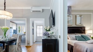 A modern living room with a black sofa, a dining table with chairs, a TV mounted on the wall, and a kitchen visible through an open door. - Flourish Apartment with Grand Terrace inside Lucca City Centre (Lucca)