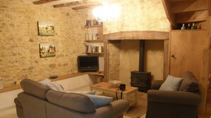 Ein gemütliches Wohnzimmer mit Steinwand, Kamin, einer Couch, einem Fernseher und einem Bücherregal.