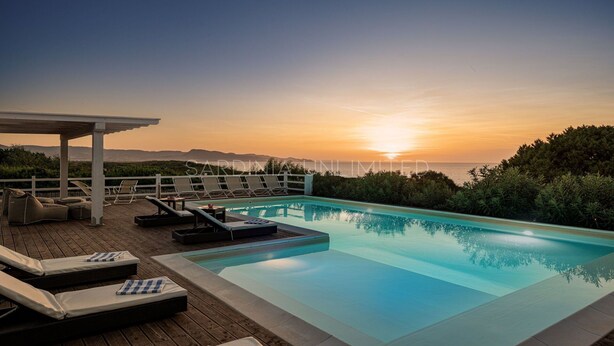 Zona junto a la piscina con sillones de descanso y una pérgola con vista al atardecer.