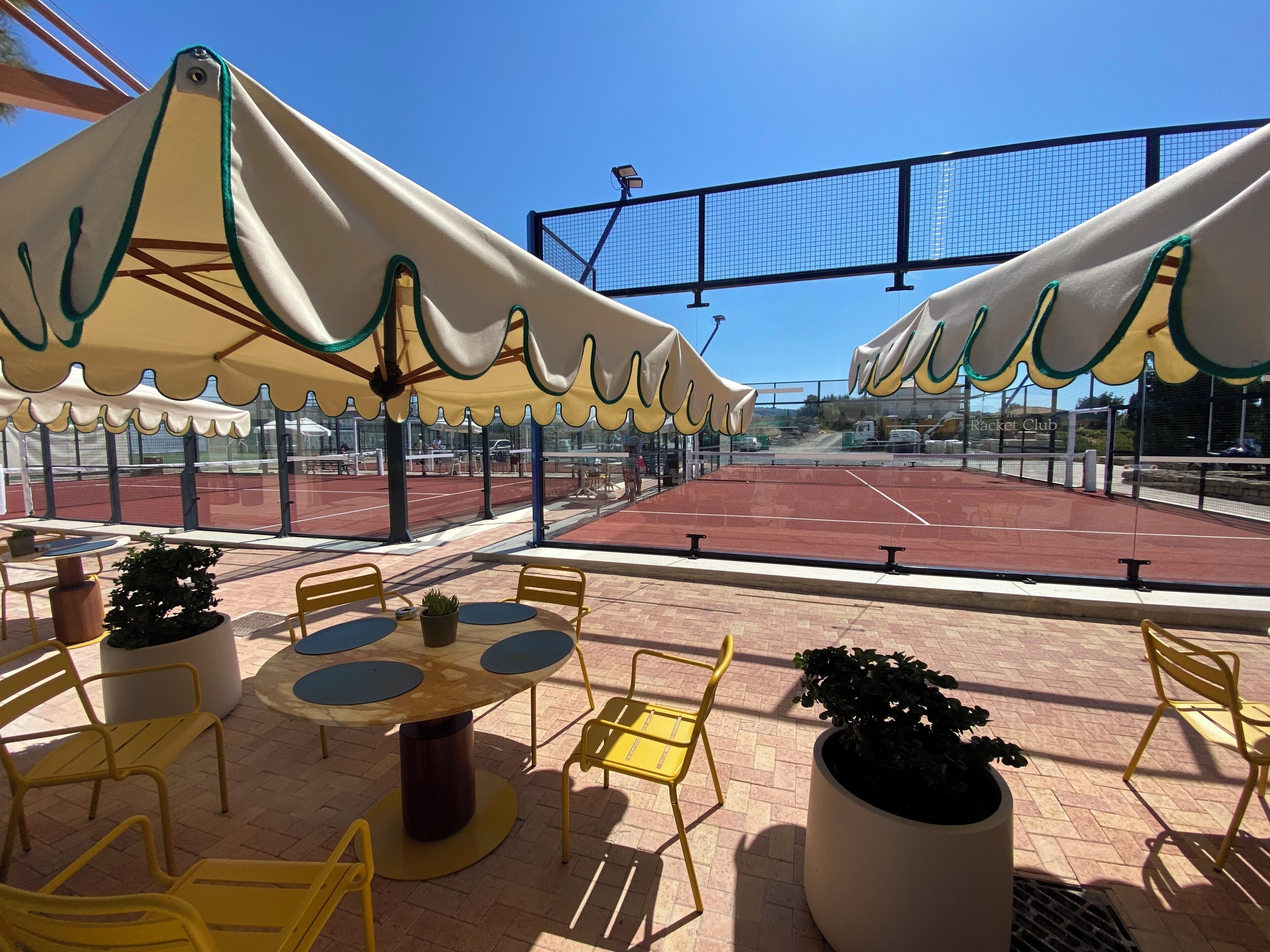 An outdoor tennis court with seating and umbrellas.