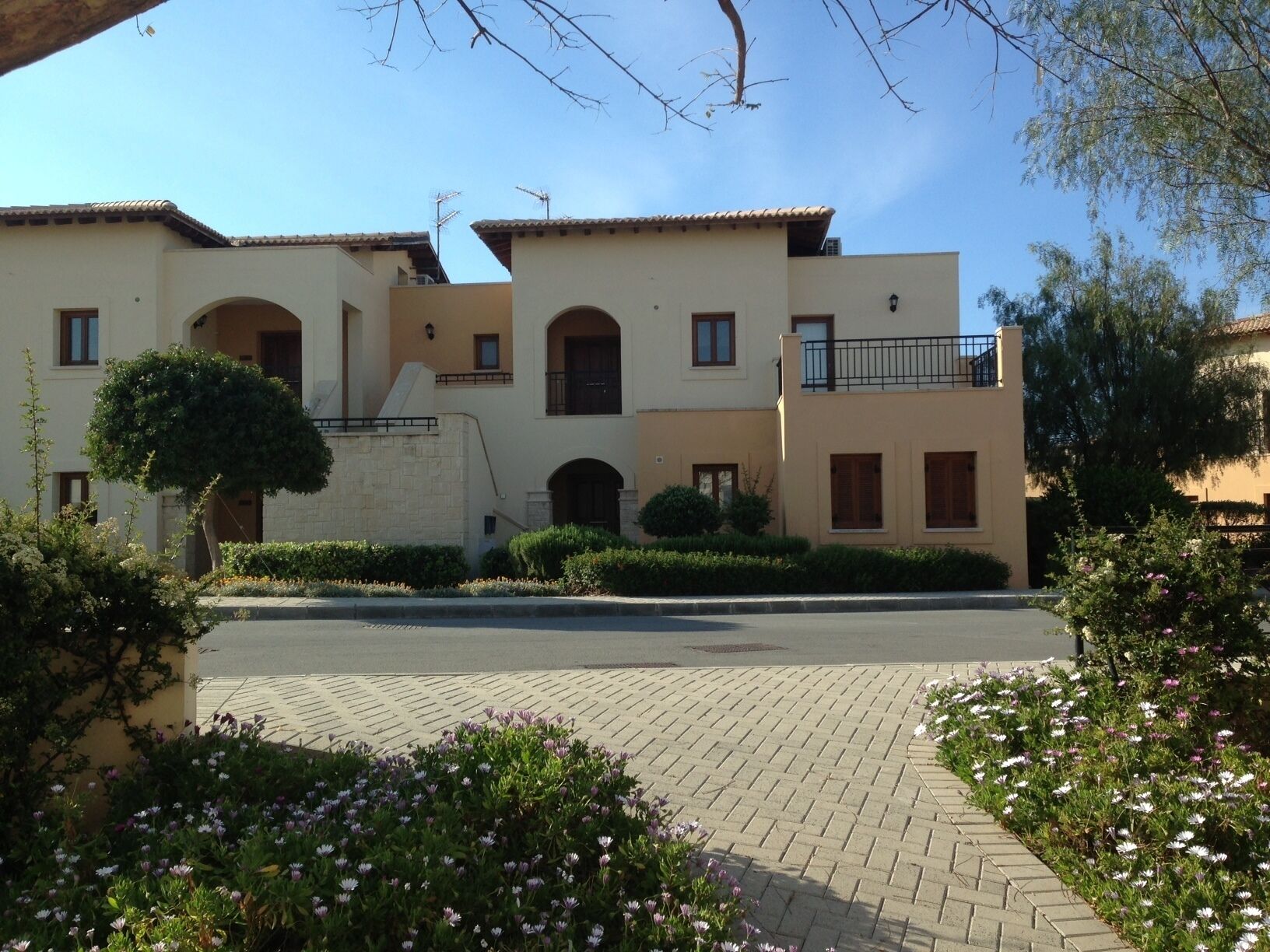 A multi-story building with a symmetrical facade, featuring a central entrance with an archway, multiple balconies, and a paved driveway.
