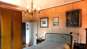 Ein Schlafzimmer mit einem großen Bett, einer hölzernen Bank, einer Pendelleuchte, einem Nachttisch, einer Lampe und einem Kleiderschrank.
