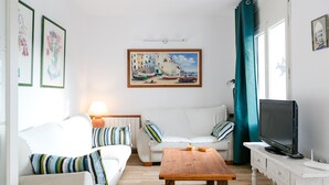 Een woonkamer met een witte bank, een houten salontafel, een televisie en kunstwerken in lijsten aan de muur.