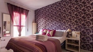 A bedroom with a large bed, a nightstand, a mirror, and a patterned wallpaper. - Sevilla best location apartment (Sevilla)