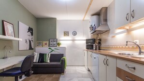 A compact kitchen with a microwave, stove, and sink. There is a small dining area with a chair and a sofa. The kitchen has white cabinets and a tiled backsplash. - Sevilla best location apartment (Sevilla)