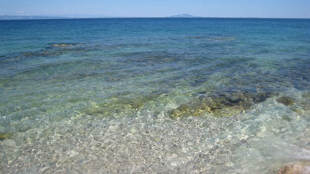 On peut voir clairement la mer, avec des rochers sous-marins visibles et une étendue de terre au loin.