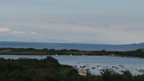 Un paysage côtier avec des bateaux sur une étendue d’eau calme, entouré de collines et de verdure.